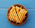 a grilled cheese toastie sliced down the centre, sitting on a round brown plate and wooden blue table